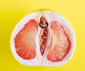 Un pamplemousse tranché en deux parties dont nous voyons une des deux moitiés qui a un piercing dans le haut en caricature d'un prix piercing clitoris ou plutôt un vertical hood piercing.