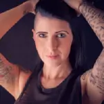 Une photo de profil d'une femme au cheveux noir avec les bras tatoués étante une cliente satisfaite de Yan Dubord Massotherapeute Perceur laissant un avis pour ses services de Body Piercing.