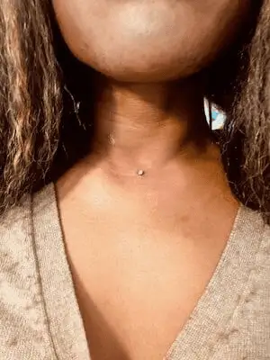 Piercing microdermal dans le devant du cou d'une femme au teint et cheveux foncé.