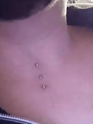 Cette photo nous montre le devant d'un cou d'une femme triplement percer par Yan Dubord montrant ses trois piercings microdermal placées à la vertical avec des bijoux avec des pierres de couleurs blanches.